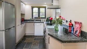 A modern kitchen with a stainless steel refrigerator, white dishwasher, and black tiled floor. - Nine Acres Barn (Marlborough)