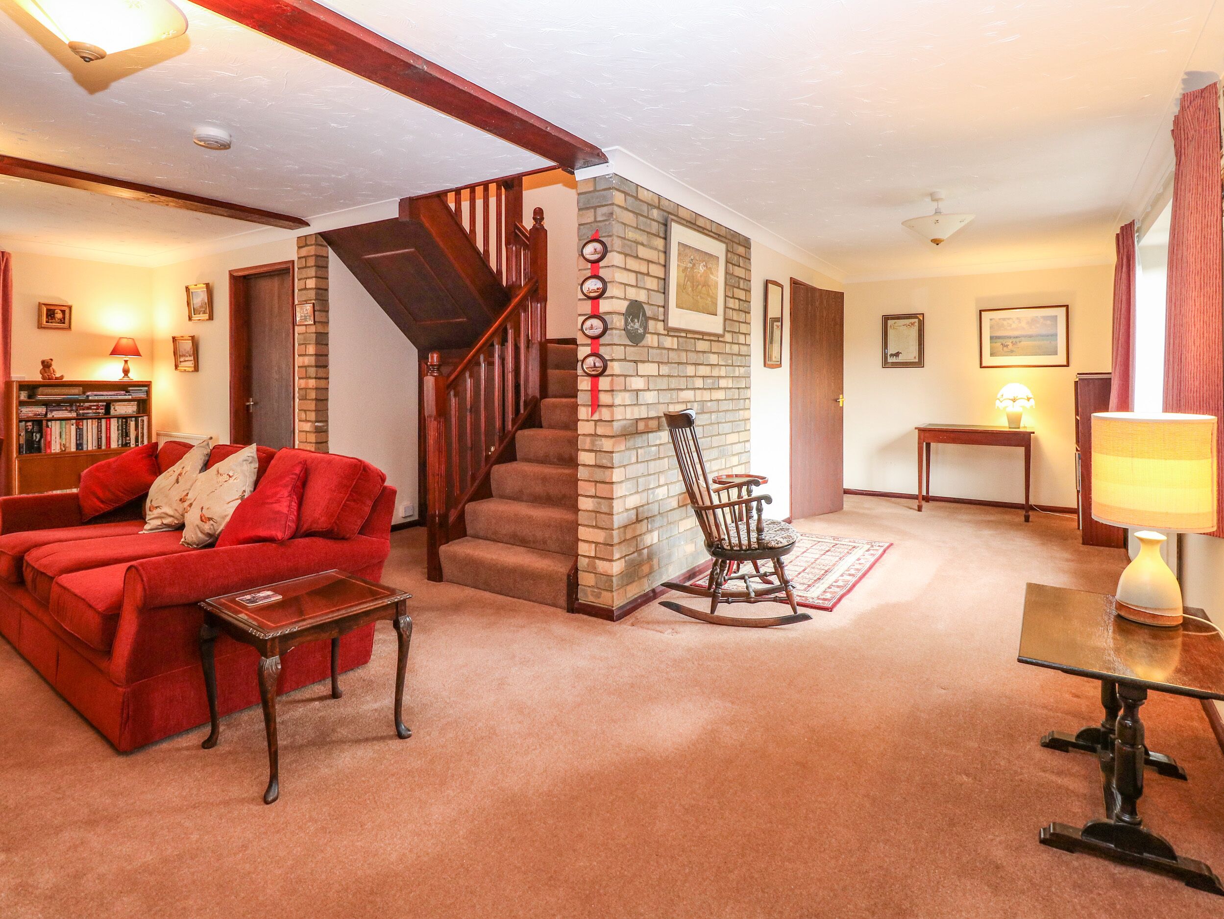 A cozy living room with a red sofa, a wooden rocking chair, a small table, and a staircase leading to another level.