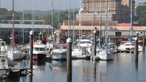 A marina with various boats docked, a large building with domed architecture in the background, and a green bridge over the water. - Pines 30 (Scarborough)
