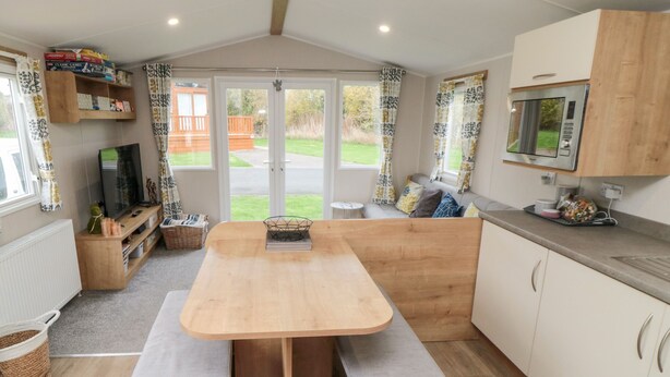A compact kitchen with a wooden table, bench seating, a microwave, and a television. - Pines 30 (Scarborough)