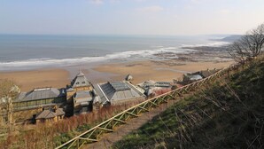 A coastal view with a beach, a wooden walkway, and a building with multiple domed structures. - Pines 30 (Scarborough)