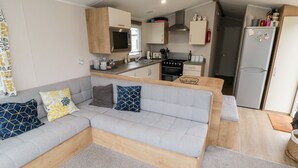 A compact living space with a grey sofa, wooden accents, a kitchenette, and a small dining area. - Pines 30 (Scarborough)