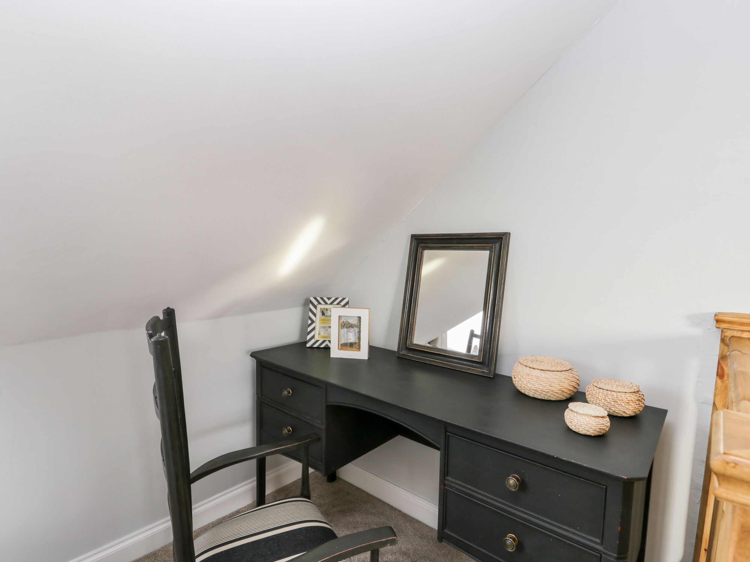 A dark wooden desk with a mirror, framed picture, and decorative baskets.