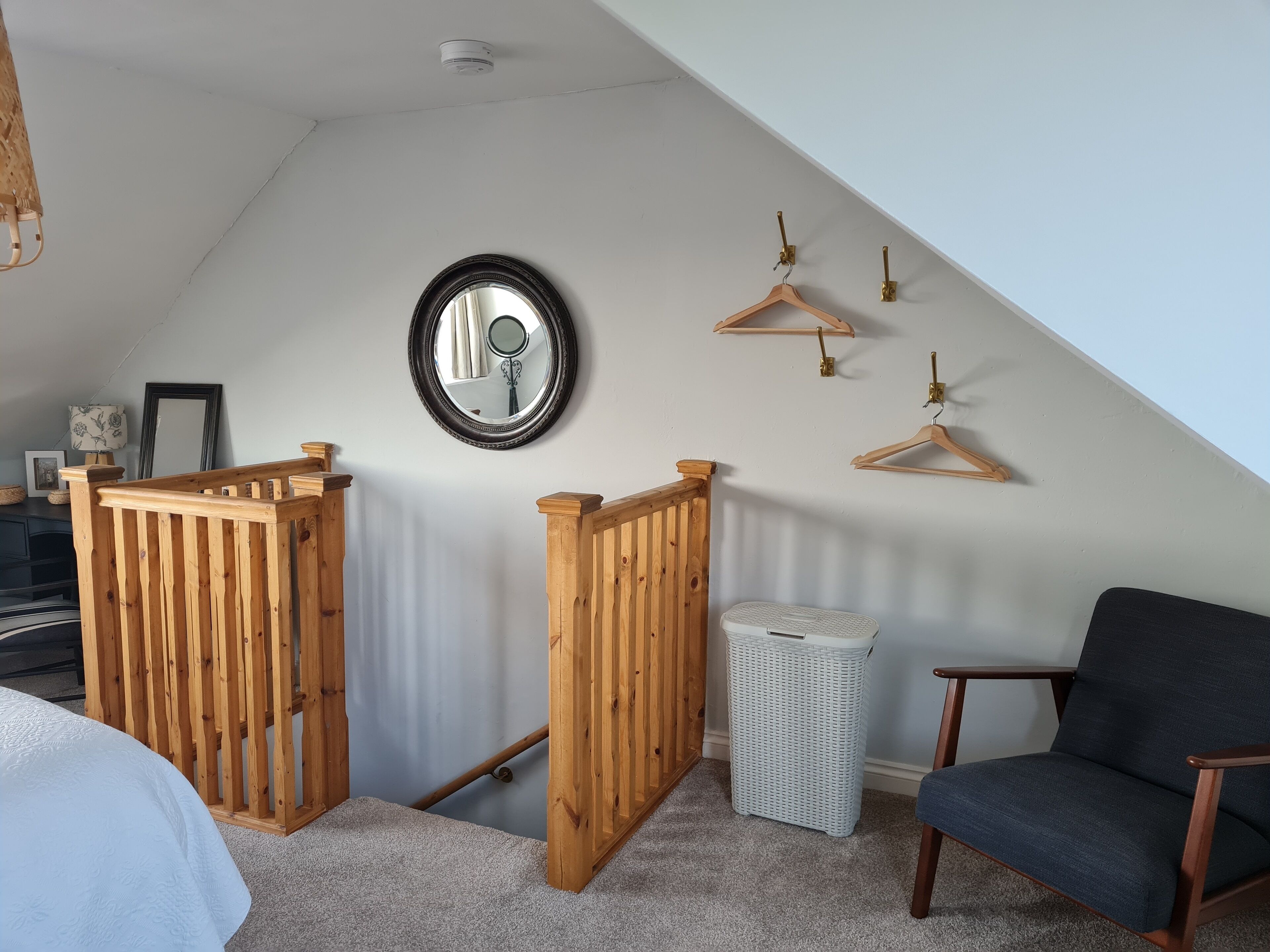 Une pièce avec un plafond en pente, des rampes en bois, un miroir et une chaise.