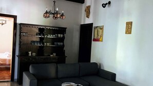 Un salon avec un canapé noir, une petite table ronde, un buffet en bois contenant de la vaisselle, un lustre et des œuvres d’art murales.