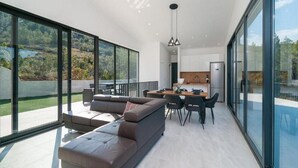 A modern living space with a large sofa, dining table, and kitchen area, featuring expansive glass walls and a view of the outdoors. - Villa Antonio - Four bedroom Villa with swimming pool (Island of Solta)