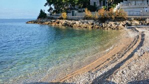 A coastal scene with a pebble beach, clear water, and buildings with stone walls and red roofs. - Villa Antonio - Four bedroom Villa with swimming pool (Island of Solta)