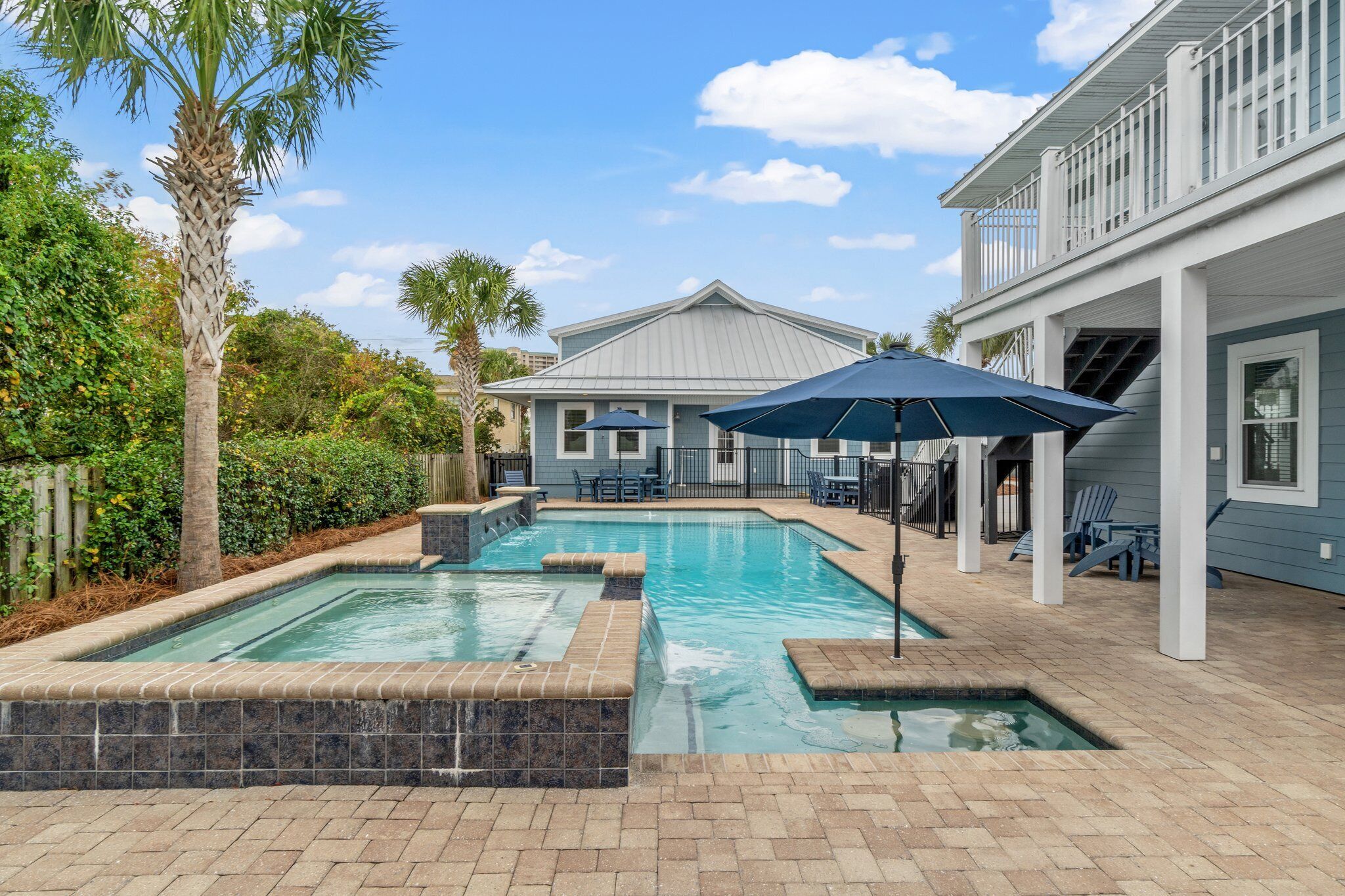 A swimming pool with a stone border, surrounded by a patio area with chairs and umbrellas.