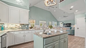 Une cuisine spacieuse avec des meubles blancs, un grand îlot central doté d’un évier et un ventilateur de plafond.