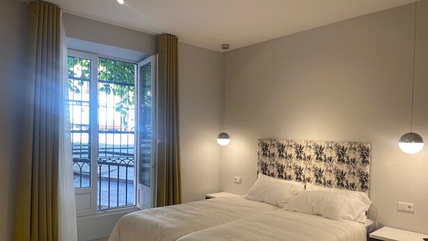 Un dormitorio con cama, mesita de noche, ventana con cortinas y vistas al exterior.