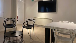 Un comedor moderno con una mesa y sillas blancas, una silla negra de diseño único, y un televisor de pantalla plana montado sobre la mesa.