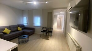 Una sala de estar moderna con un sofá gris, dos cojines amarillos, una mesita redonda y un televisor montado en la pared.