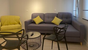 Un salón con un sofá gris, cojines amarillos, un sillón amarillo y una mesa de centro redonda con un control remoto.