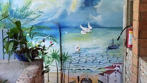 Une fresque représentant une scène de plage avec des bateaux et un goéland, un pilier de pierre et un escalier menant à un niveau supérieur.