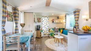 A modern living room with a dining area, featuring a wooden dining table, chairs, a sofa, and a coffee table. - Little John Mobil Home (Fréjus)