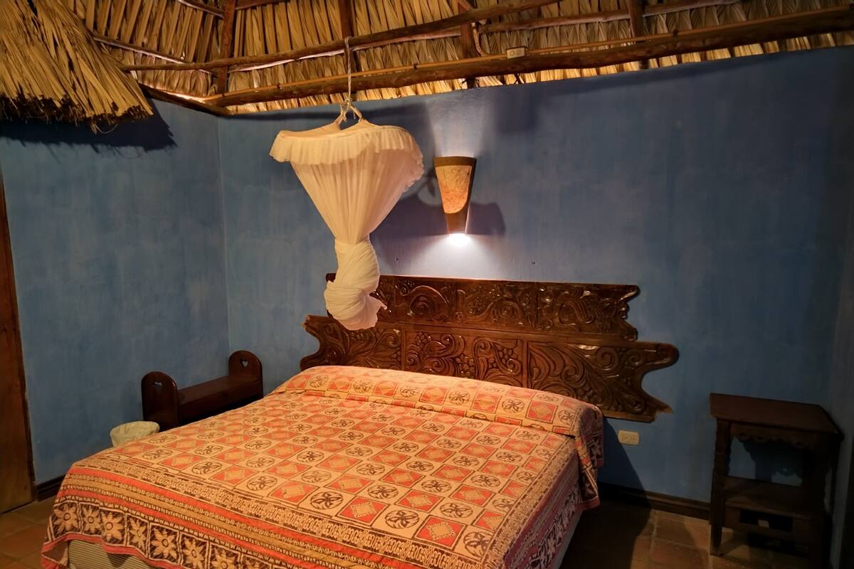 A room with a bed, a hanging mosquito net, a wall-mounted light, and a wooden headboard.