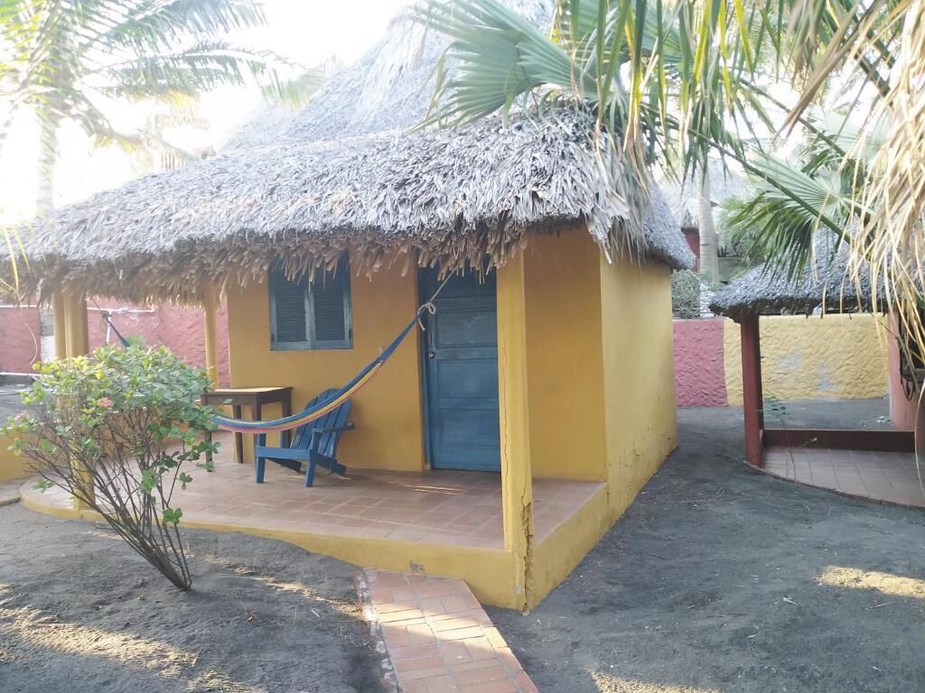 A small yellow building with a thatched roof, a blue door, and a hammock outside.