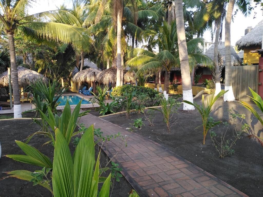 A tropical garden with a pool, palm trees, and thatched-roof structures.