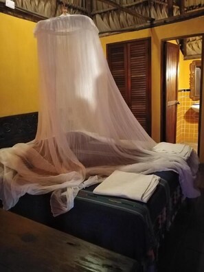 A bed with a mosquito net, a wooden bench, and a tiled wall. - HOTEL PEZ DE ORO (Taxisco)