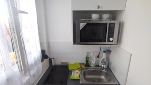 Een kleine keuken met een magnetron, spoelbak en een keukenkastje.
