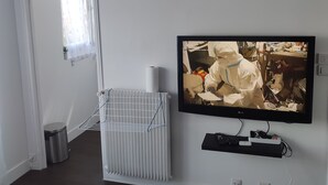 Een woonkamer met een zwarte wandklok, een wandtelevisie, een radiator en een deur naar een andere kamer.