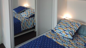 Een slaapkamer met een spiegelkast, twee bedden met beddengoed met een patroon, en bedlampen.