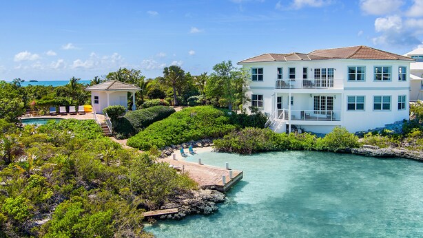 A large, multi-story building with a balcony, surrounded by lush greenery and a clear blue sky. - Seaside Villa, Beachfront Paradise (Providenciales)