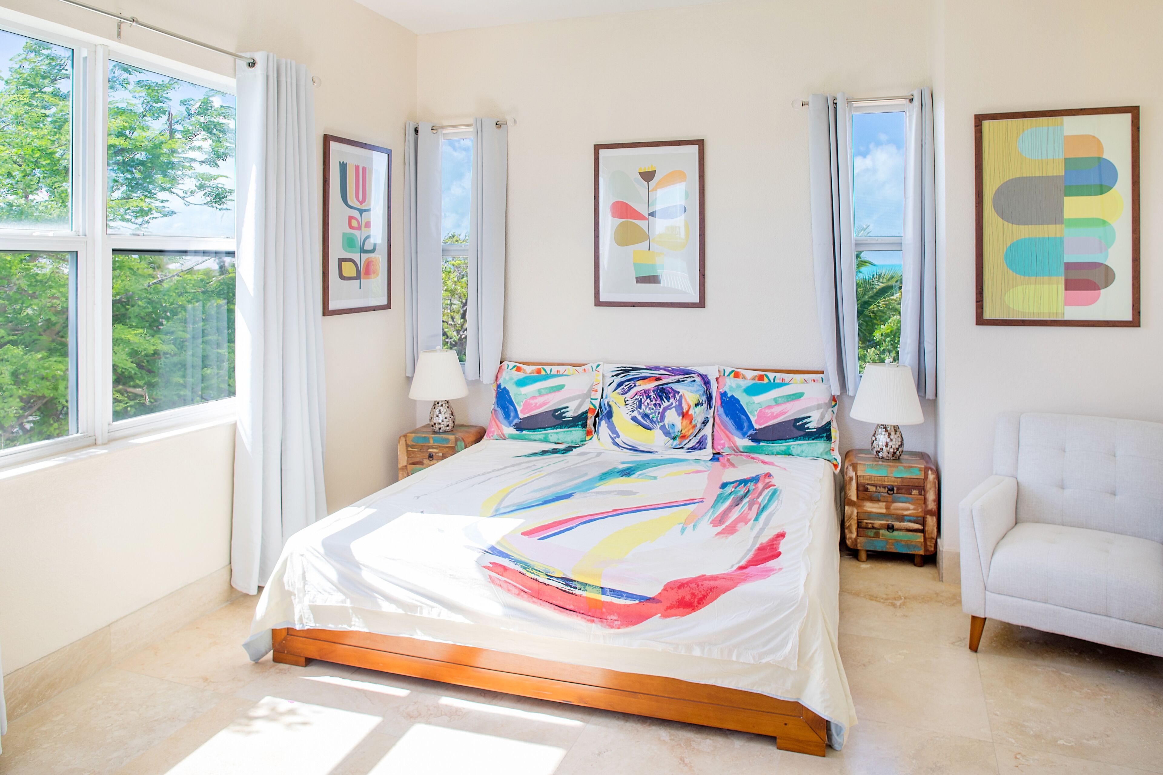 Une chambre à coucher avec un grand lit, deux tables de chevet, une chaise et des œuvres d’art accrochées aux murs.