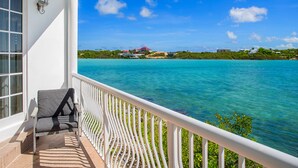 A balcony with a view of turquoise waters and a distant island with buildings. - Seaside Villa, Beachfront Paradise (Providenciales)