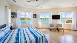 A hotel room with a bed, two chairs, a TV, and large windows with a view of the sea. - Seaside Villa, Beachfront Paradise (Providenciales)