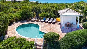 A swimming pool with a curved edge, surrounded by a brick patio, and a gazebo with a tiled roof. - Seaside Villa, Beachfront Paradise (Providenciales)