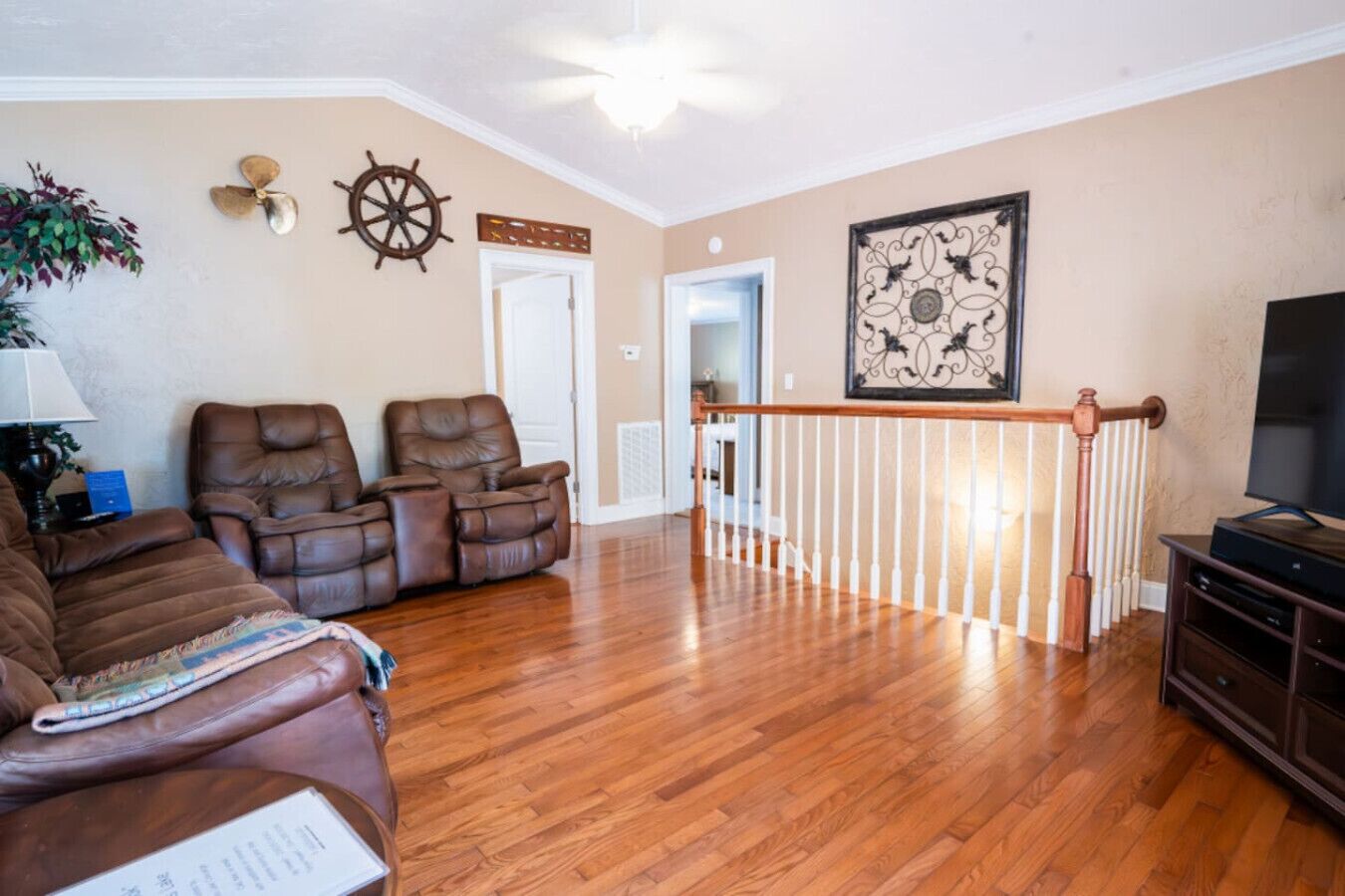 Een woonkamer met een houten vloer, twee bruine leren fauteuils, een bruine bank, een televisie en een decoratief kunstwerk aan de muur.