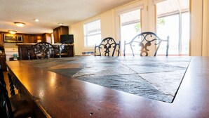 Ruime eetruimte met een lange tafel en stoelen, grote ramen en een keuken op de achtergrond.