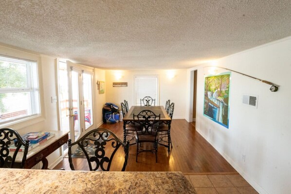 A dining area with a wooden table and chairs, a painting on the wall, and a window with blinds.
