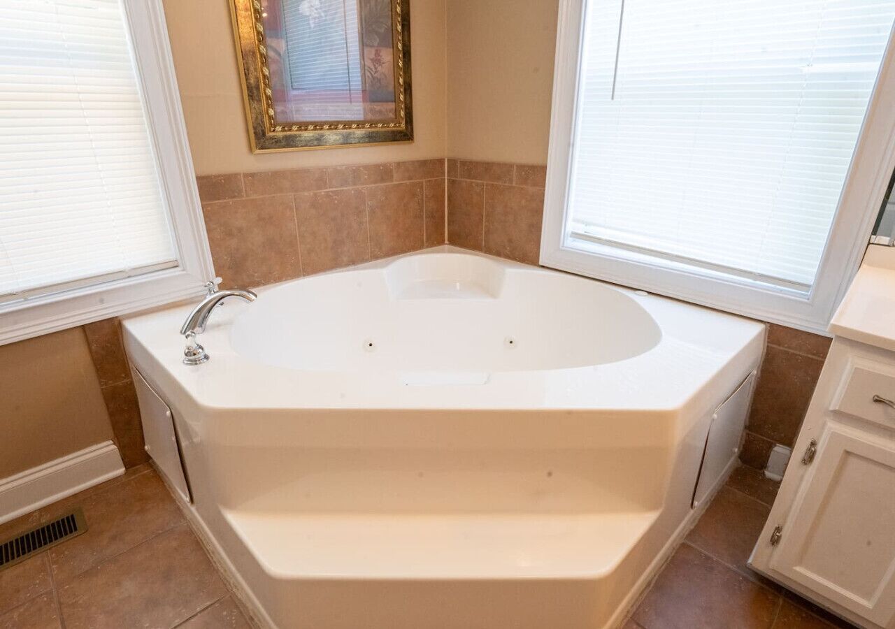 Une salle de bain avec une baignoire sur pieds, une fenêtre avec des stores et un tableau encadré au mur.