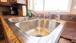 Een rvs spoelbak met een dubbele kraan, een fles afwasmiddel en een rek voor keukenpapier.