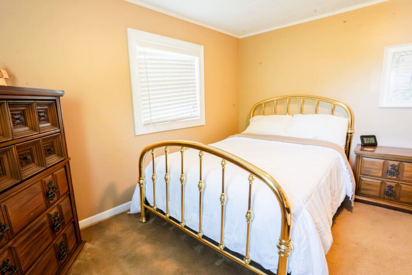 A bedroom with a bed, wooden dresser, and a nightstand with a clock.