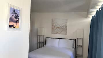 Hotelkamer met een bed, twee bedlampen, een plafondventilator, een foto van palmbomen en een schilderij van abstracte lijnen.
