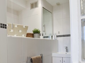 Ein Badezimmer mit weiß gefliesten Wänden, einem Spiegel, einem Handtuchhalter, einem Waschbecken und Pflegeprodukten auf der Ablagefläche.