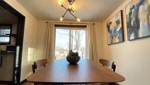 A dining area with a wooden table, four chairs, a ceiling fan, and two abstract paintings on the wall. - Designer Home in Walkable Historic Greendale (Greendale)