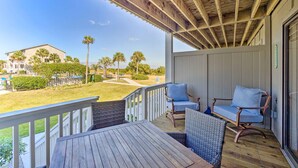 Una terraza de madera con mobiliario de mimbre y vista a una zona residencial con palmeras.