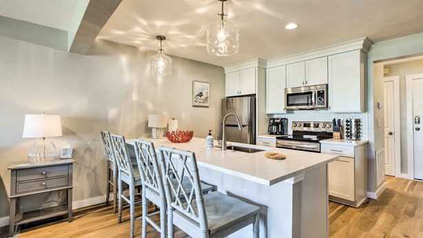 Una cocina moderna con una isla central, taburetes de bar, un refrigerador, un microondas y un lavabo.