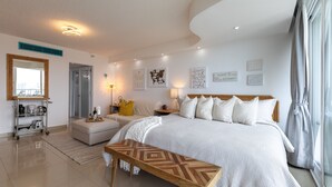 Une chambre à coucher moderne avec un grand lit, un banc en bois, une table de chevet et une étagère fixée au mur.