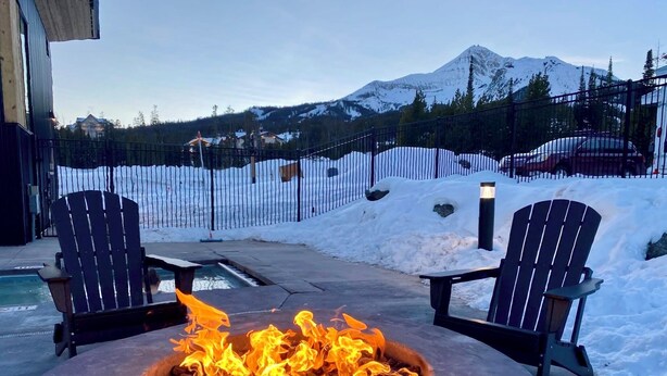A fire pit with two Adirondack chairs in a snowy outdoor area with a mountain view.