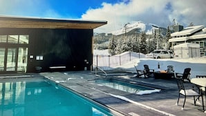 A pool area with a view of snow-covered mountains and a building with large windows.