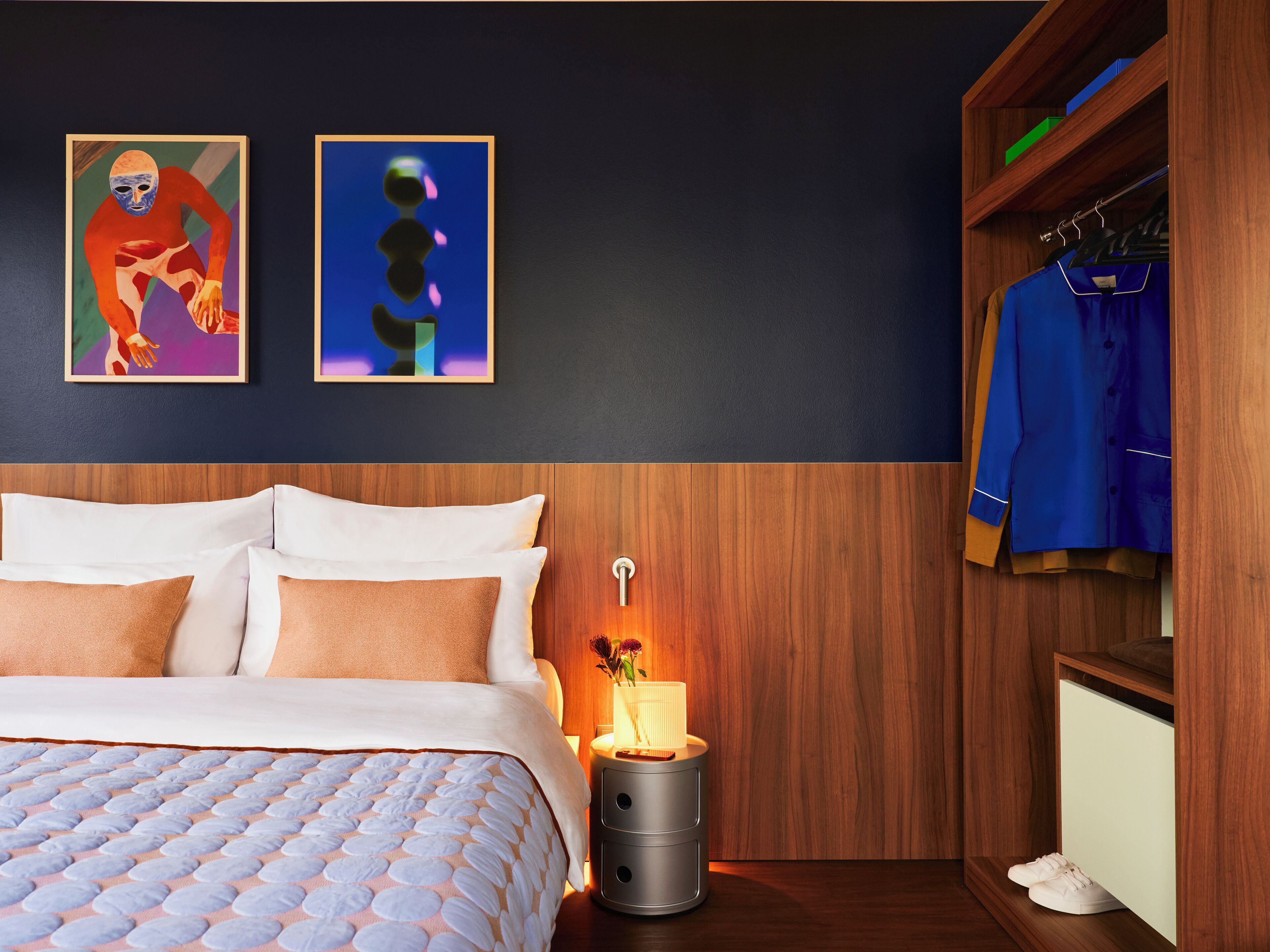 Una camera da letto con un letto, cuscini, un comodino con una lampada e un armadio con abiti.