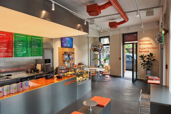 Un café moderno con una barra que exhibe diferentes productos alimenticios y una pizarra con bebidas y opciones de desayuno.