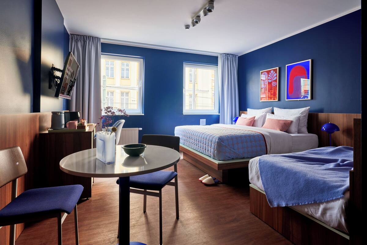 A modern hotel room with a bed, a desk, a chair, and a window with curtains.