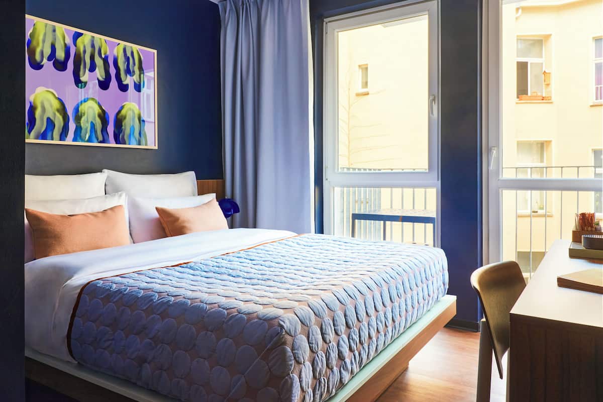 A hotel room with a large bed, a desk, and a window with a view of buildings.