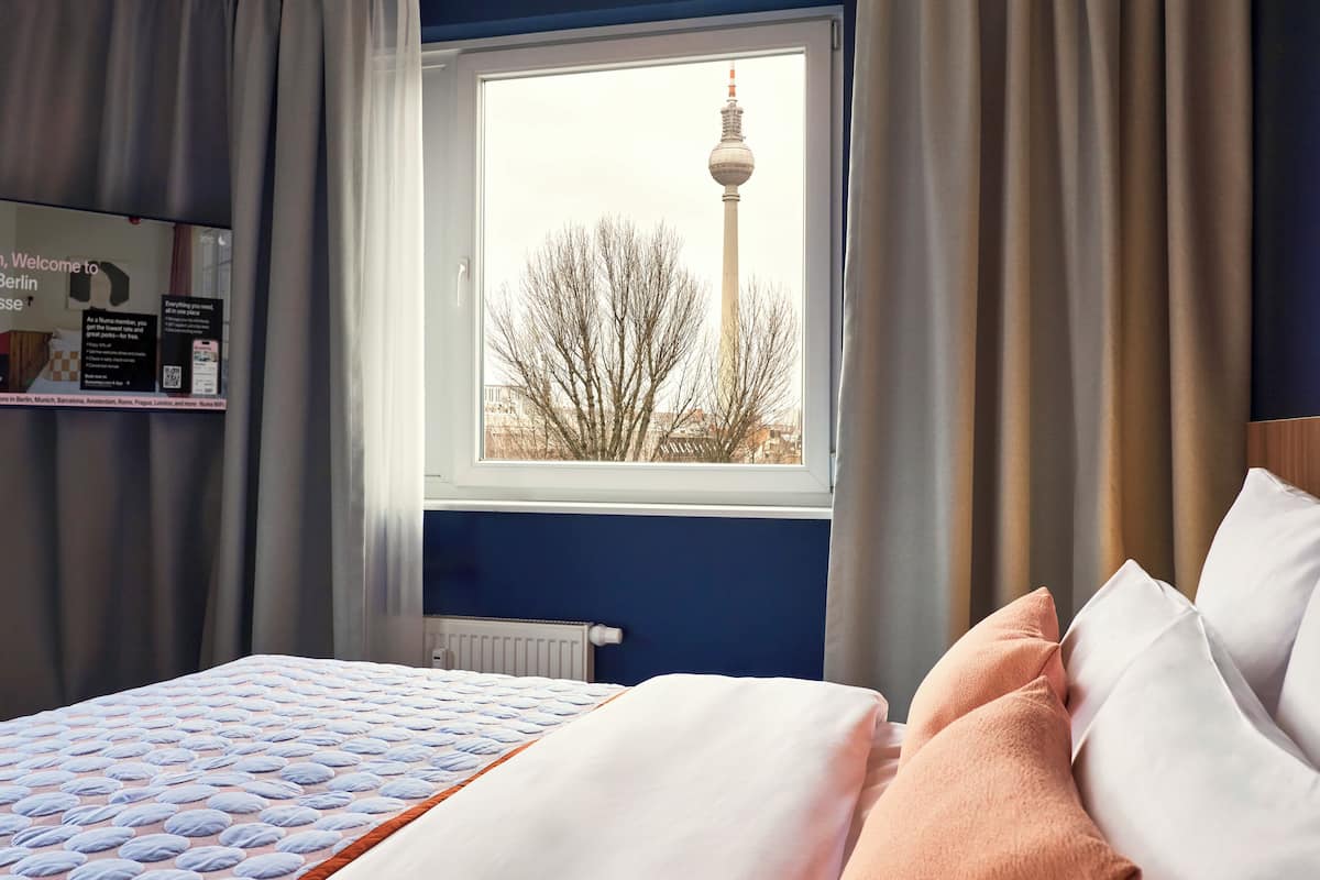 A hotel room with a bed, a window with a view of a tower, and a sign on the wall.